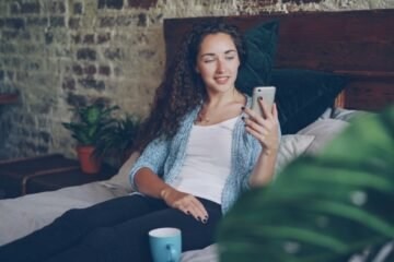 AWL meaning in text captured by a woman reacting warmly to a message on her phone in bed