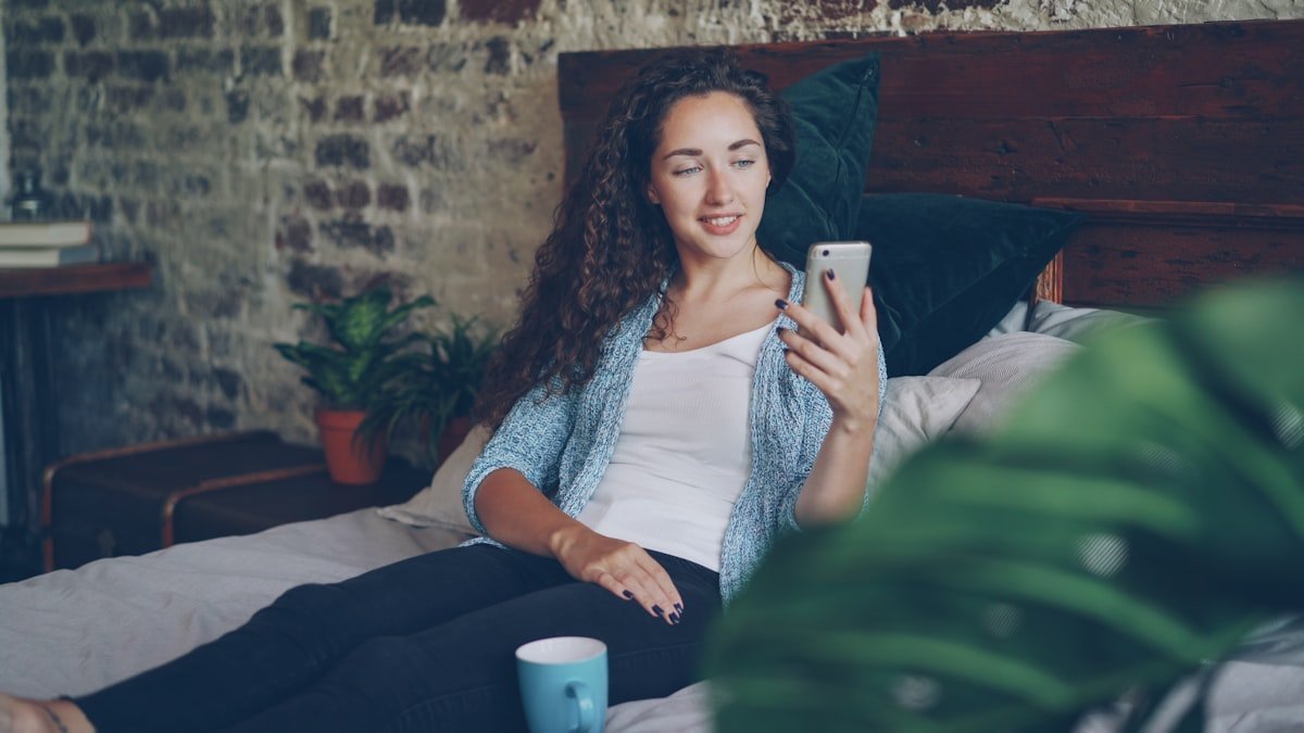 AWL meaning in text captured by a woman reacting warmly to a message on her phone in bed
