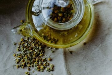 Chamomile meaning illustrated by dried chamomile flower heads spilled beside a glass teapot of golden infusion