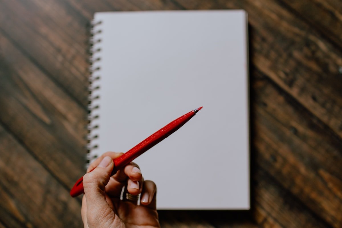 Comma before or after however illustrated by a red editing pen held over a blank notebook page