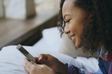 HYS meaning in text shown by a woman in bed smiling at a good-morning message on her phone