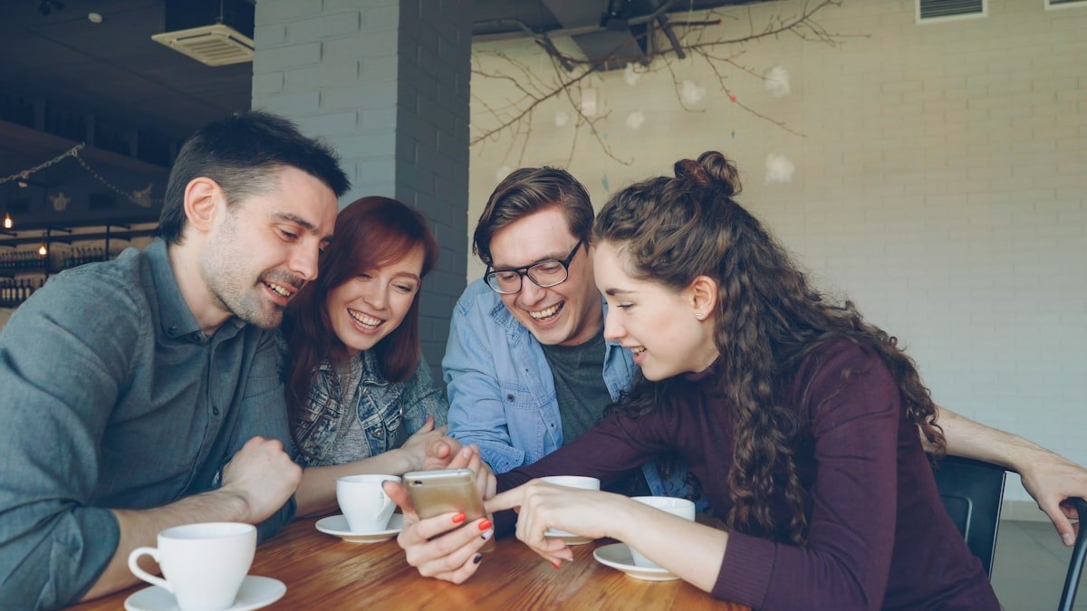 JT meaning in text shown by four friends laughing at a teasing message on a phone in a cafe