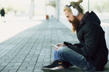 Lummy meaning slang looked up on a phone by a listener with headphones sitting on a city sidewalk