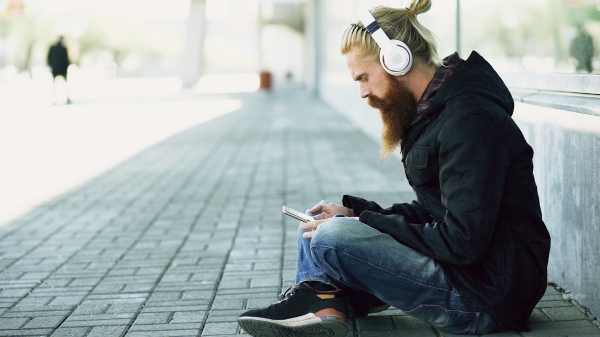 Lummy meaning slang looked up on a phone by a listener with headphones sitting on a city sidewalk