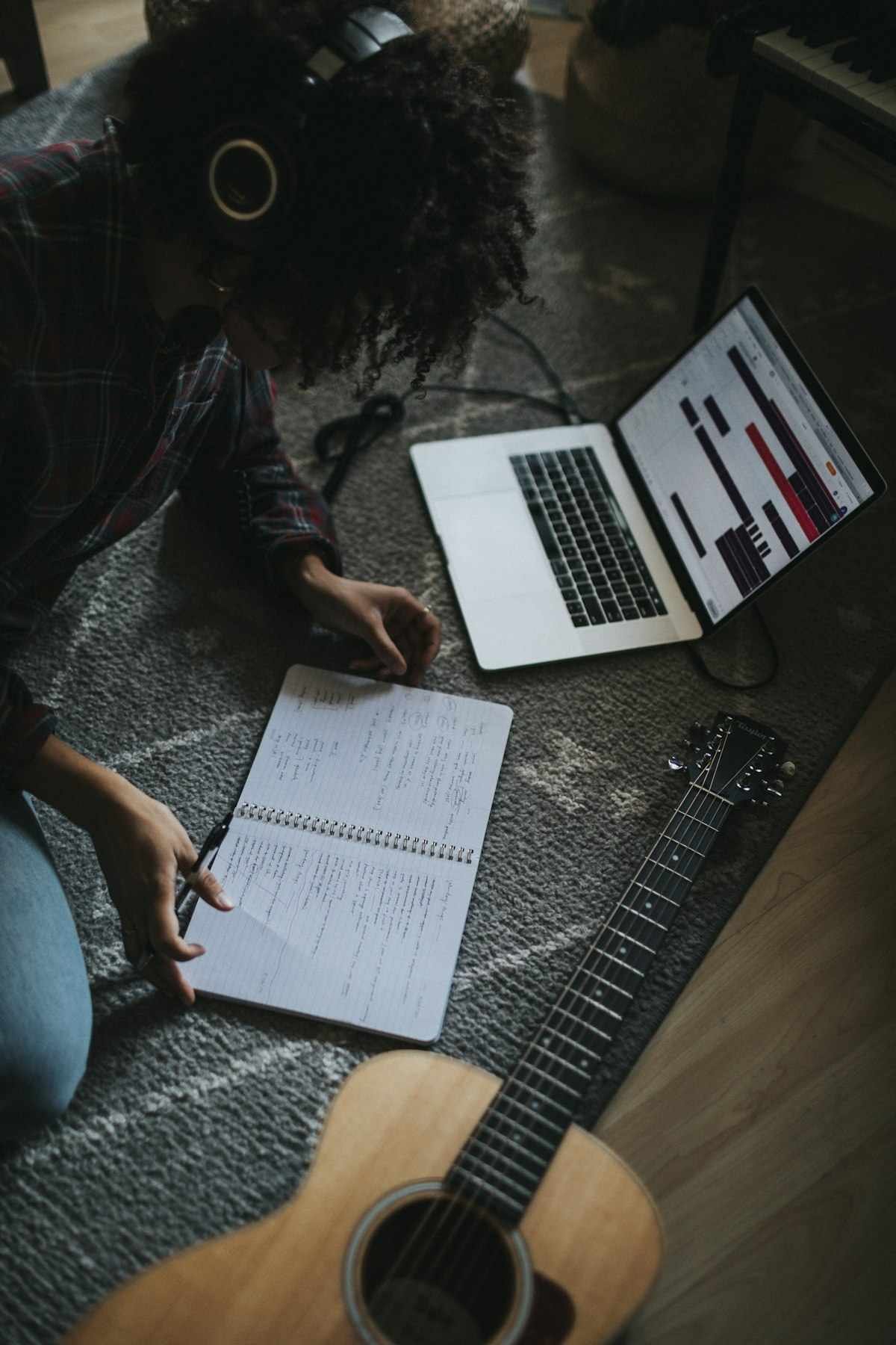 Metaphors for songs being drafted by a songwriter with headphones, notebook, laptop and guitar on the floor