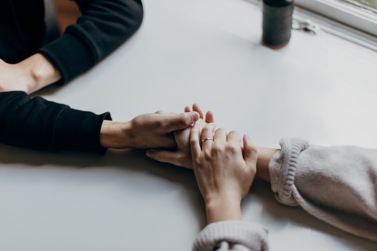 What to say when people pass away shown by two people holding hands across a table in quiet support