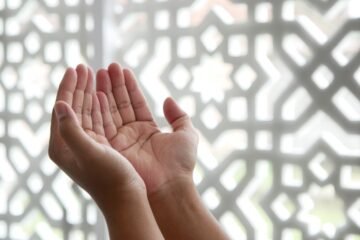 What to say when someone dies in Islam shown by open cupped hands raised in dua before a geometric screen