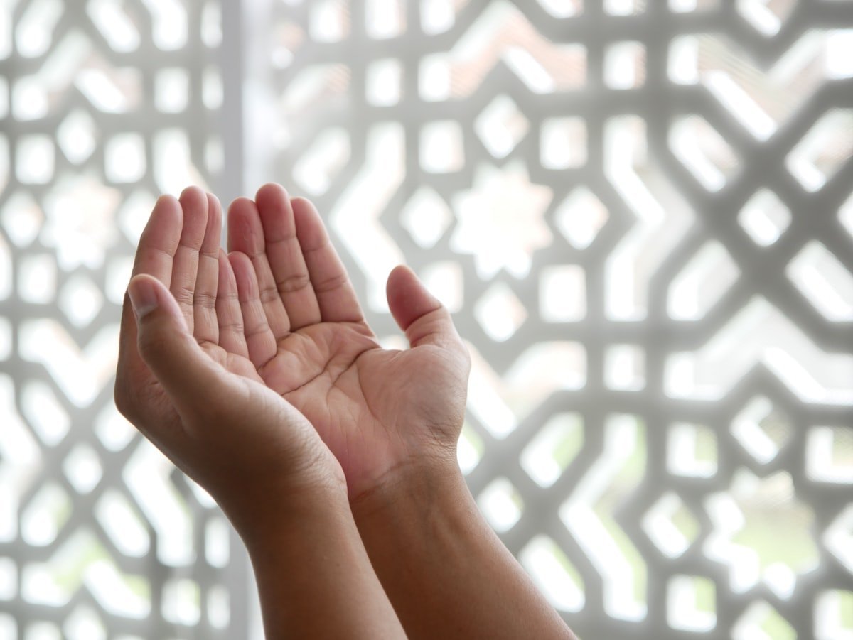 What to say when someone dies in Islam shown by open cupped hands raised in dua before a geometric screen